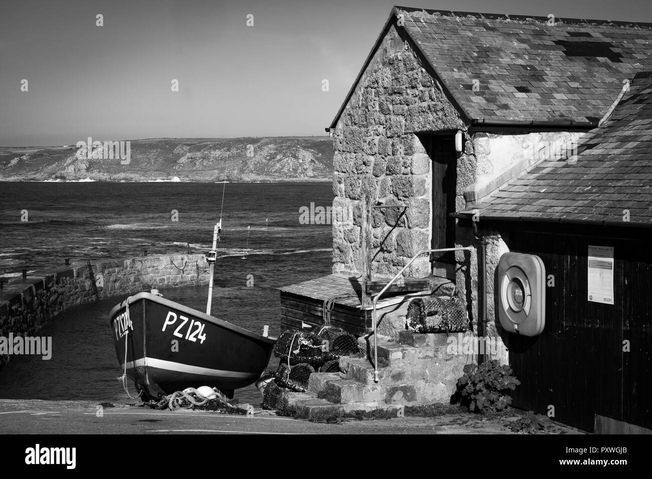 Image en noir et blanc de bateau de pêche échoués sur le Sennen Cove de halage à côté des bâtiments du vieux port et des marches en pierre. Banque D'Images