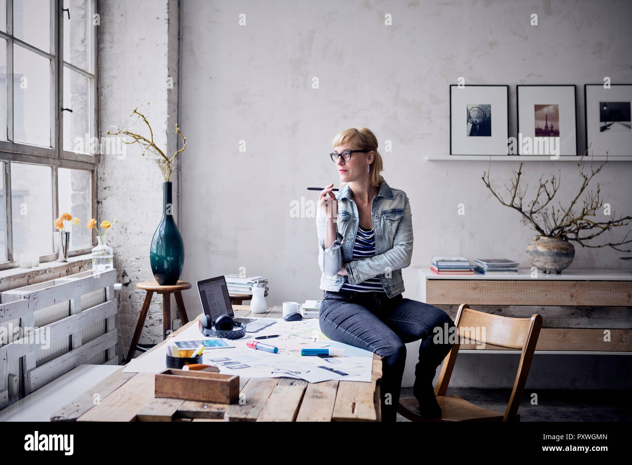 Woman sitting on desk in loft à la recherche d'une fenêtre Banque D'Images