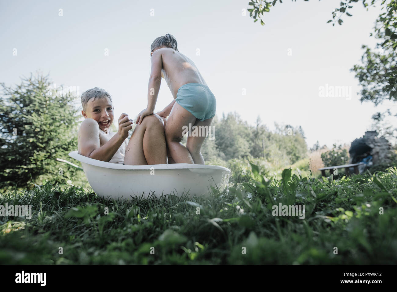 Frère et sœur jouant avec de l'eau dans la petite baignoire dans jardin Banque D'Images