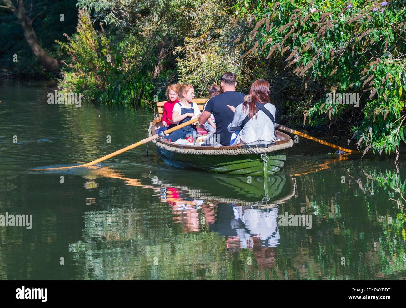 Famille dans un petit bateau à rames montrant des reflets dans l'eau sur un canal en automne, au Royaume-Uni. Banque D'Images