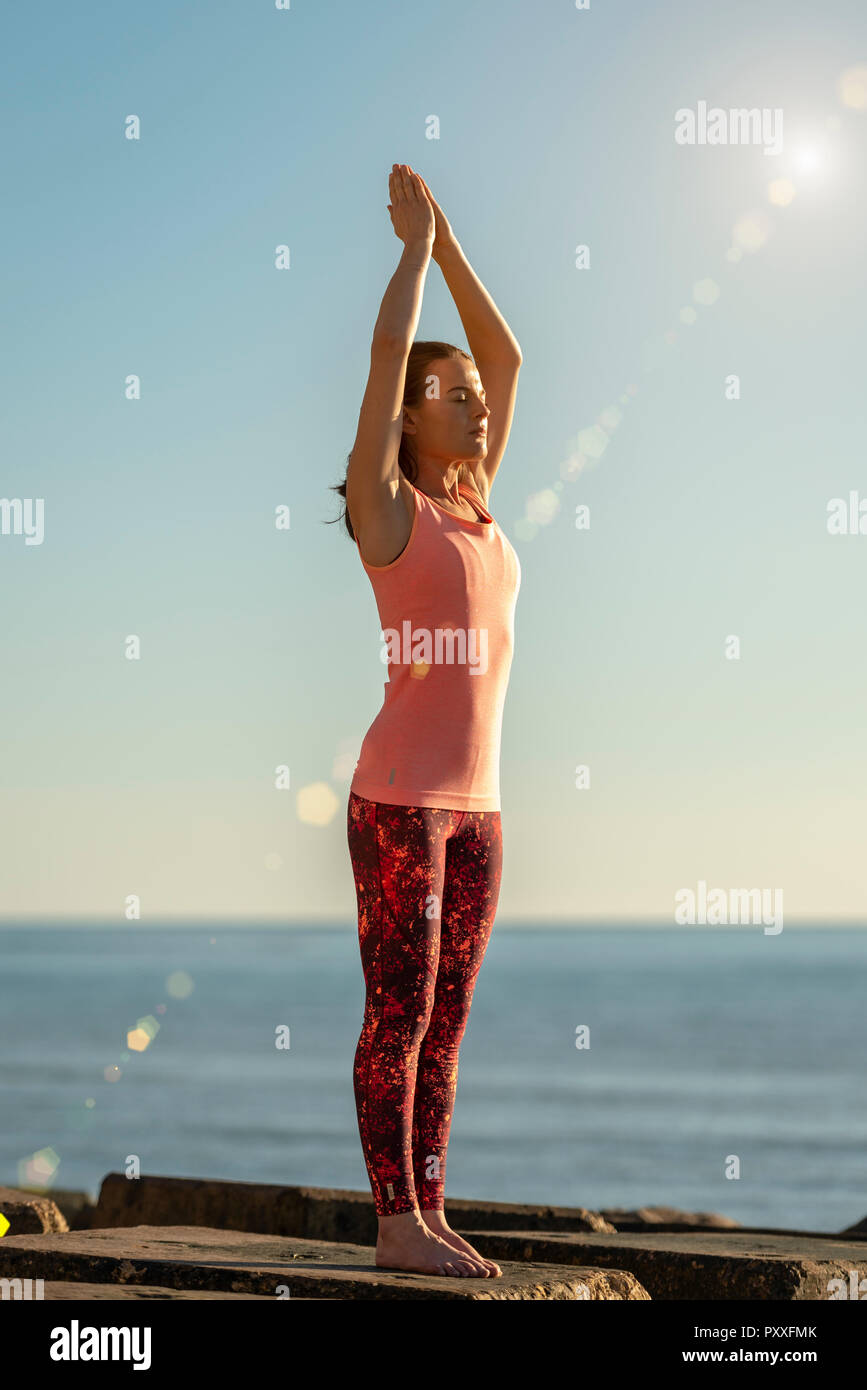 Femme debout par la mer pratiquant le yoga, posture de l'arbre, Banque D'Images