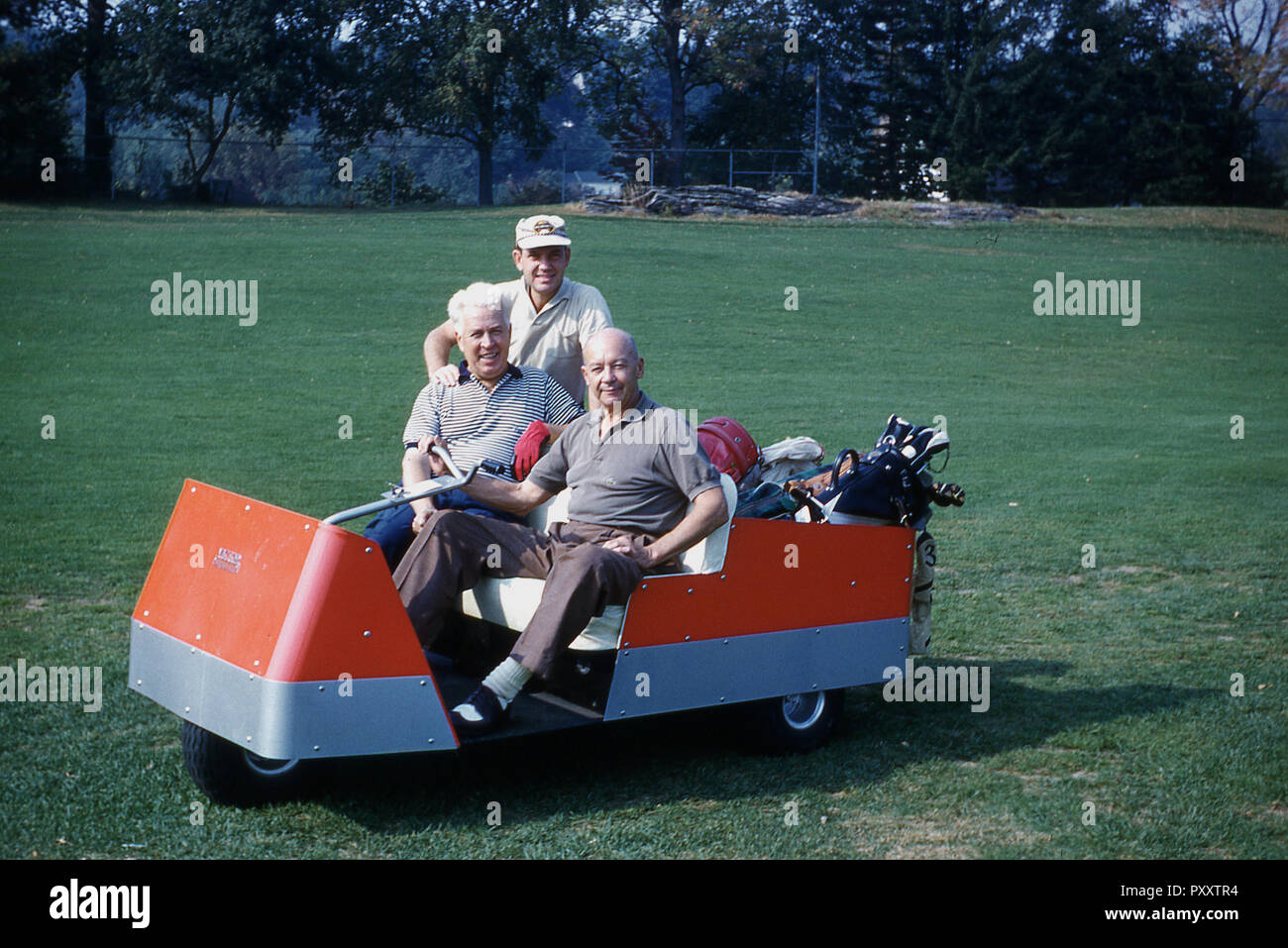 Années 70, deux golfeurs masculins assis dans un trois-roues de chariot de golf électrique, avec un timon, le contrôle de la direction, USA. C'est dans les années 1950 que le chat ou d'un kart de golf a commencé à devenir plus populaire auprès des golfeurs, en particulier les personnes âgées plus joueurs. Les premières voitures de golf électriques ont été utilisés sur les terrains de golf avec un terrain assez plat comme leurs batteries ont une durée de vie courte. Banque D'Images