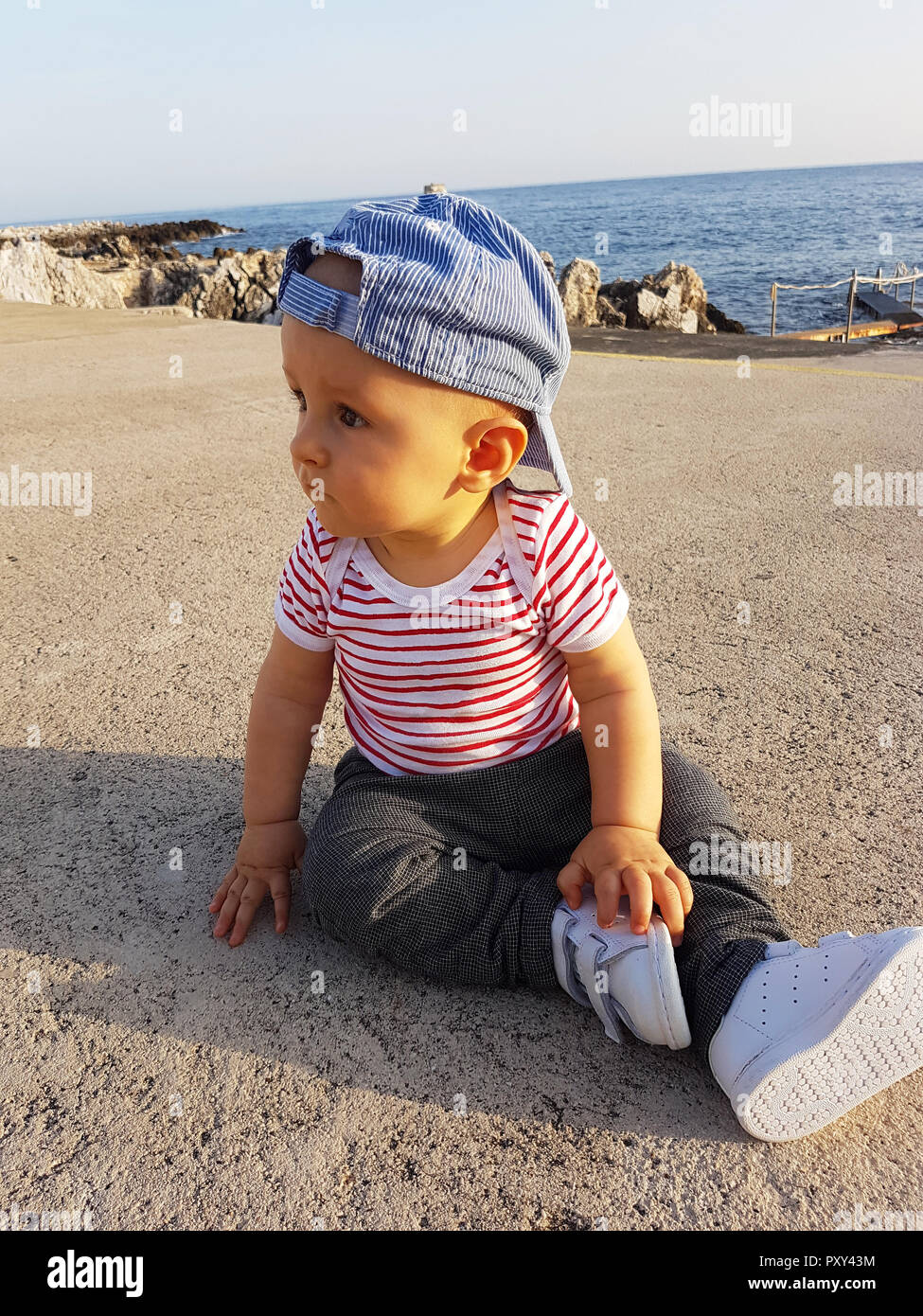Mignon Bébé Garçon 1 ans portant une casquette à l'envers et les vêtements  à rayures, Portrait. La mer Méditerranée en arrière-plan Photo Stock - Alamy