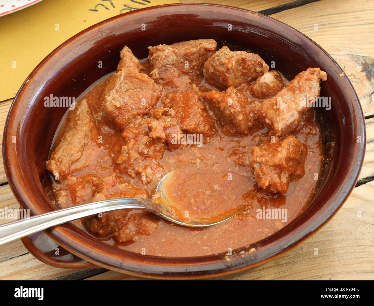 Un bol brun sur une table en bois avec une cuillère contenant un ragoût de boeuf dans une sauce tomate et épices pour manger avec de la polenta, un plat typiquement italien Banque D'Images