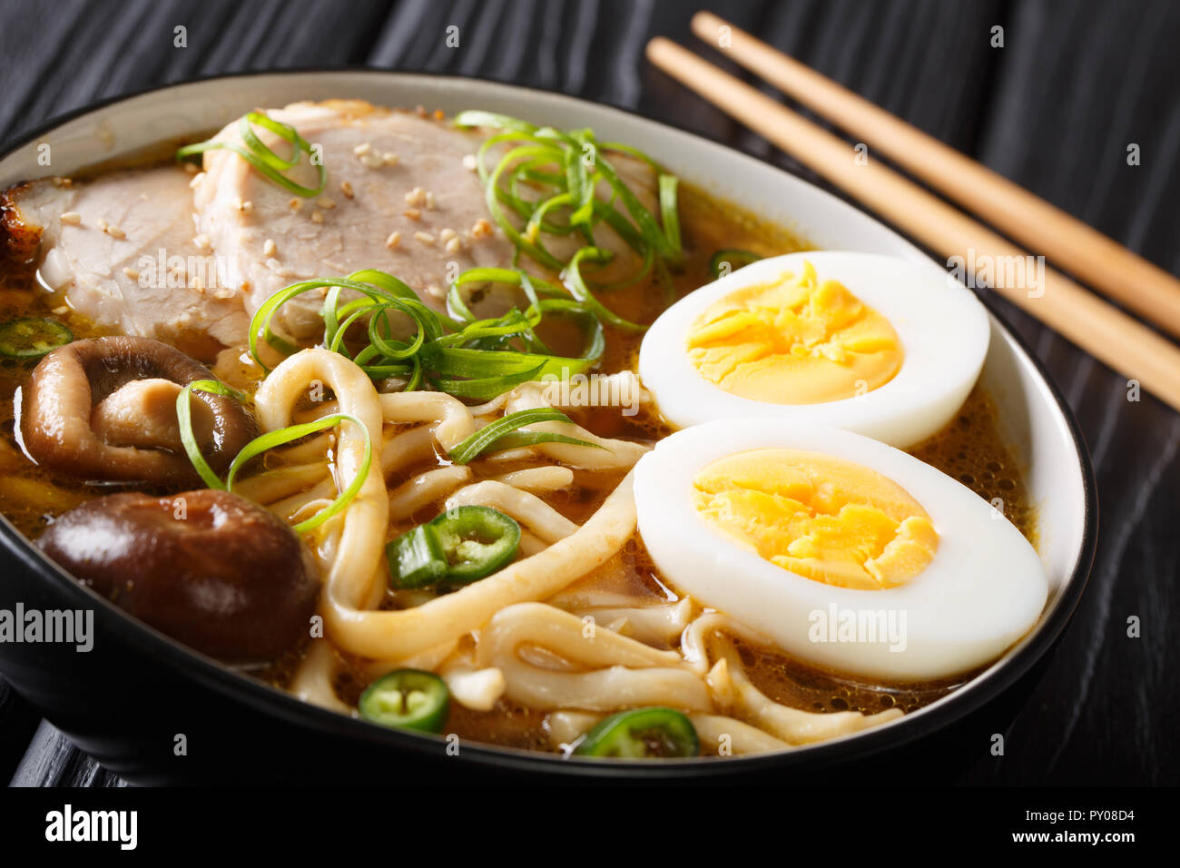 Soupe de nouilles Udon épicé, porc, œufs durs, oignons et champignons shiitake close-up dans un bol sur la table horizontale. Banque D'Images