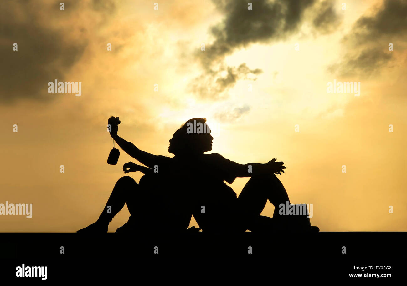Vue de côté et silhouette de couple assis dos à dos au coucher du soleil et prendre des selfies Banque D'Images