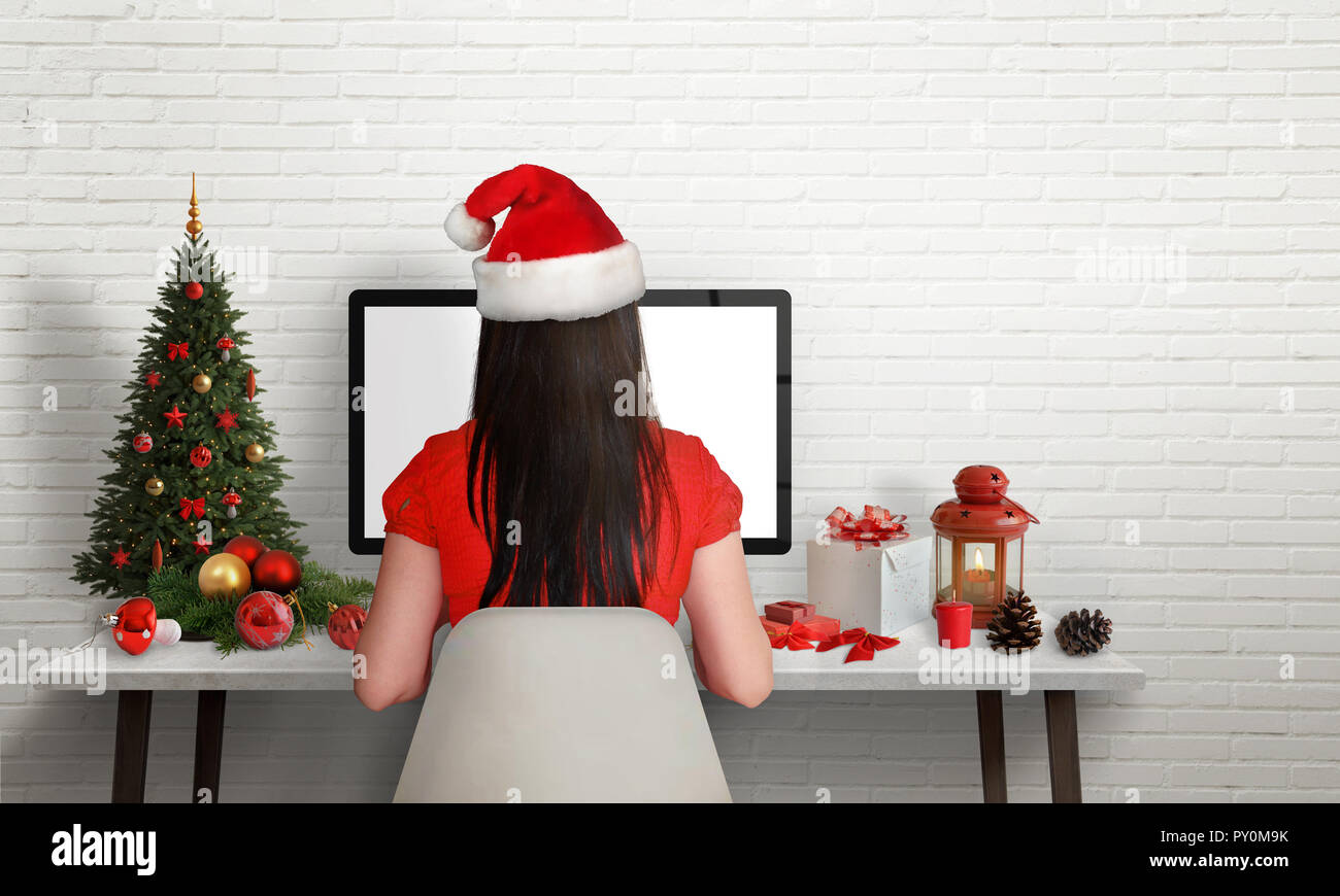 Fille avec Santa's hat travailler sur ordinateur à l'époque de Noël. À côté de l'espace libre sur mur de brique pour le texte. Banque D'Images