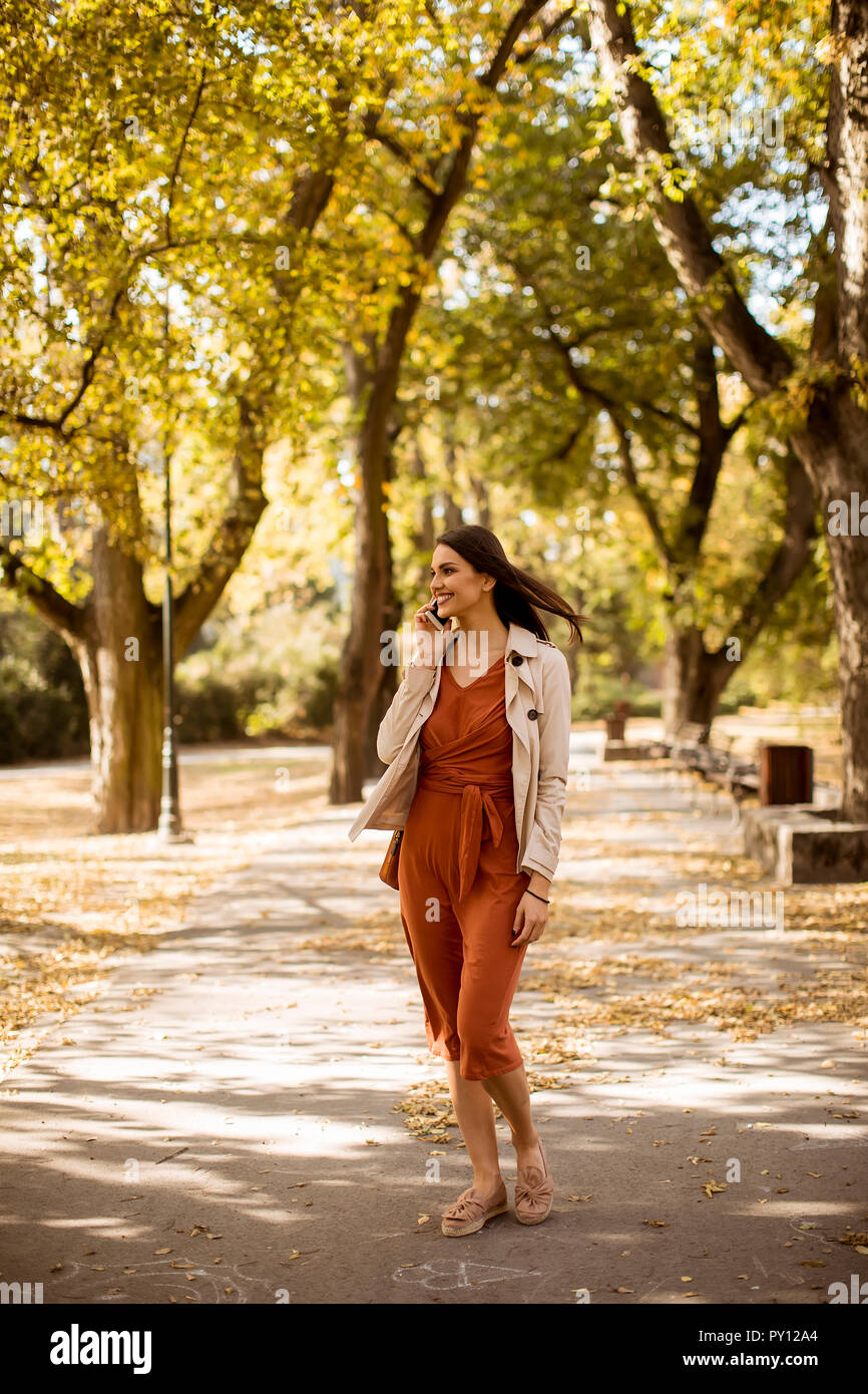Happy young woman using cell phone in autumn park sur belle journée Banque D'Images
