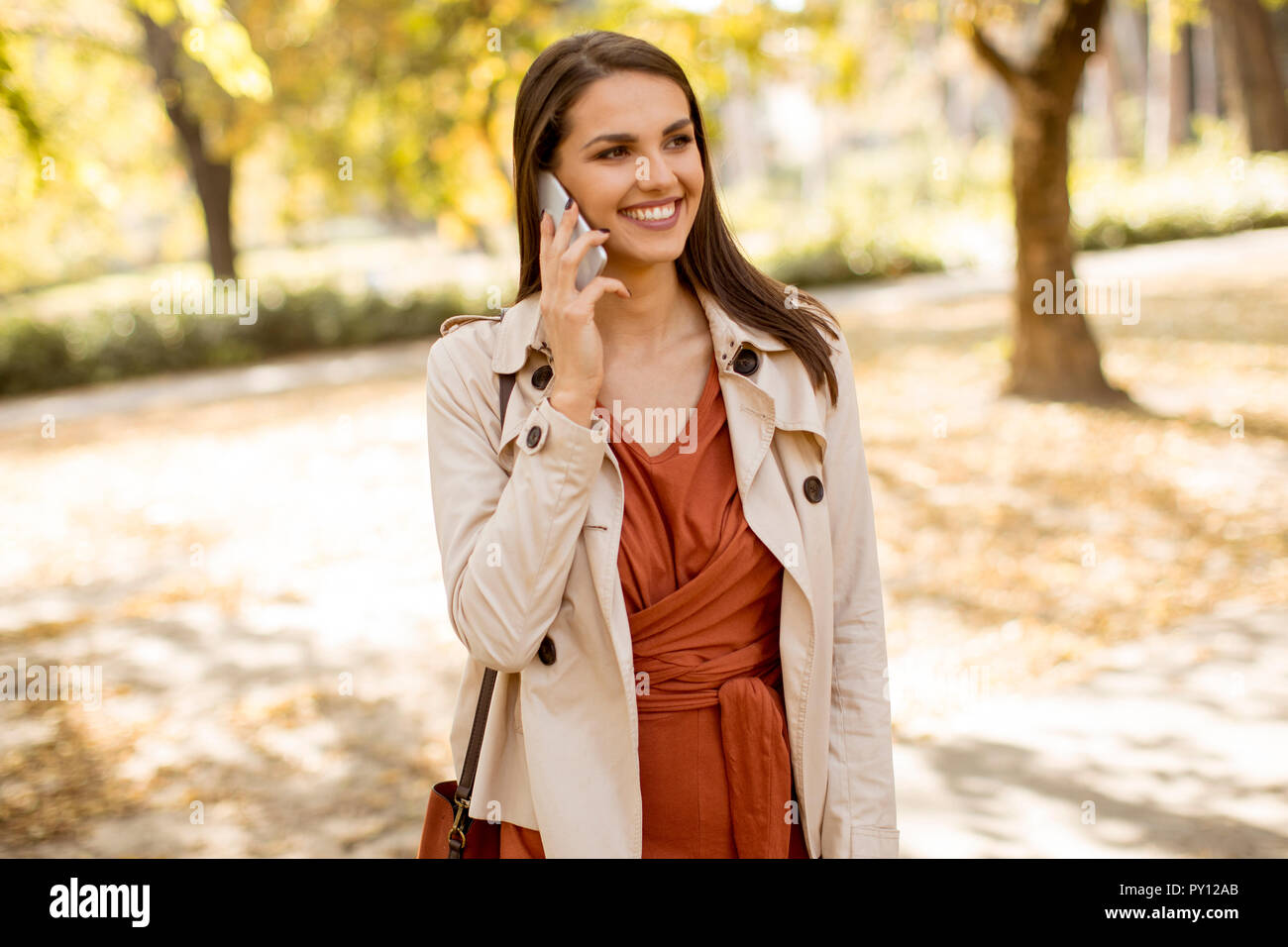 Happy young woman using cell phone in autumn park sur belle journée Banque D'Images