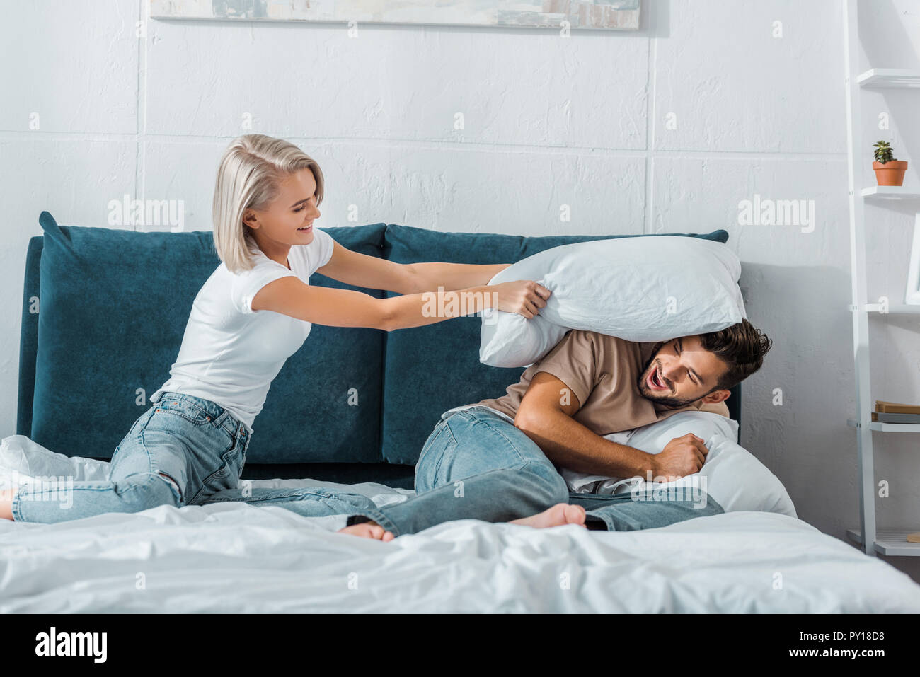 Petite amie heureux de battre petit ami avec oreiller sur le lit dans la  chambre Photo Stock - Alamy