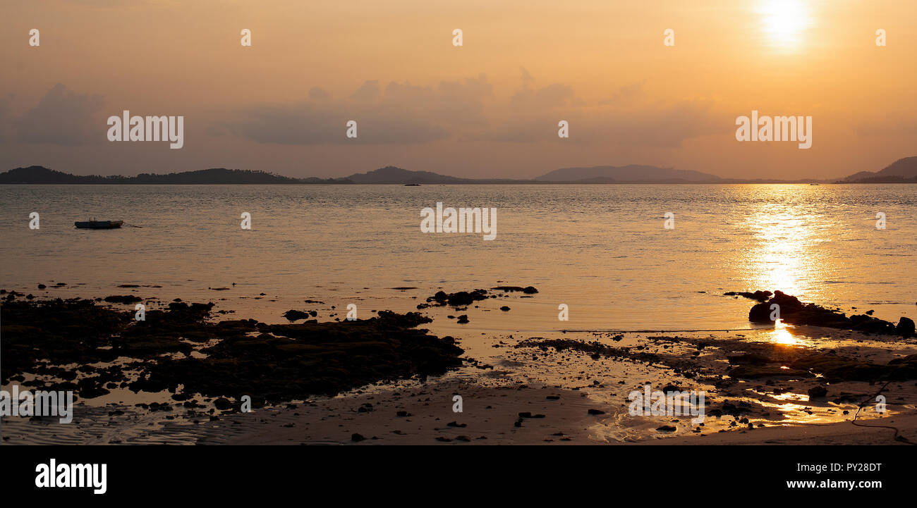 Coucher du soleil dans un cadre tropical sur la mer sur un rivage rocailleux et dans la distance peut être vu îles de faible altitude. Le ciel est rouge et d'or brillant. Banque D'Images