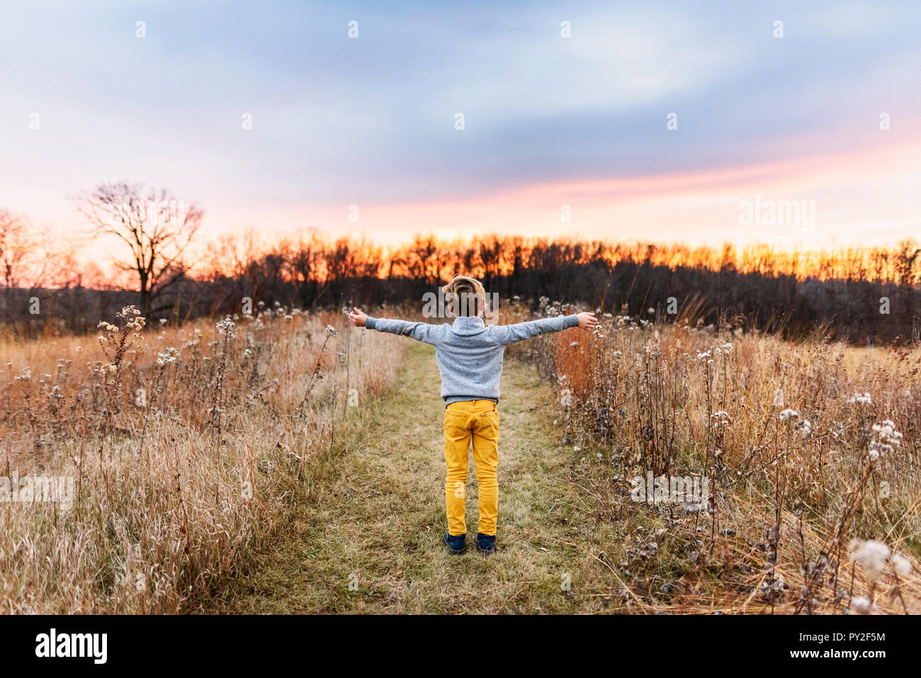 Garçon debout dans un champ au coucher du soleil avec ses bras tendus, United States Banque D'Images