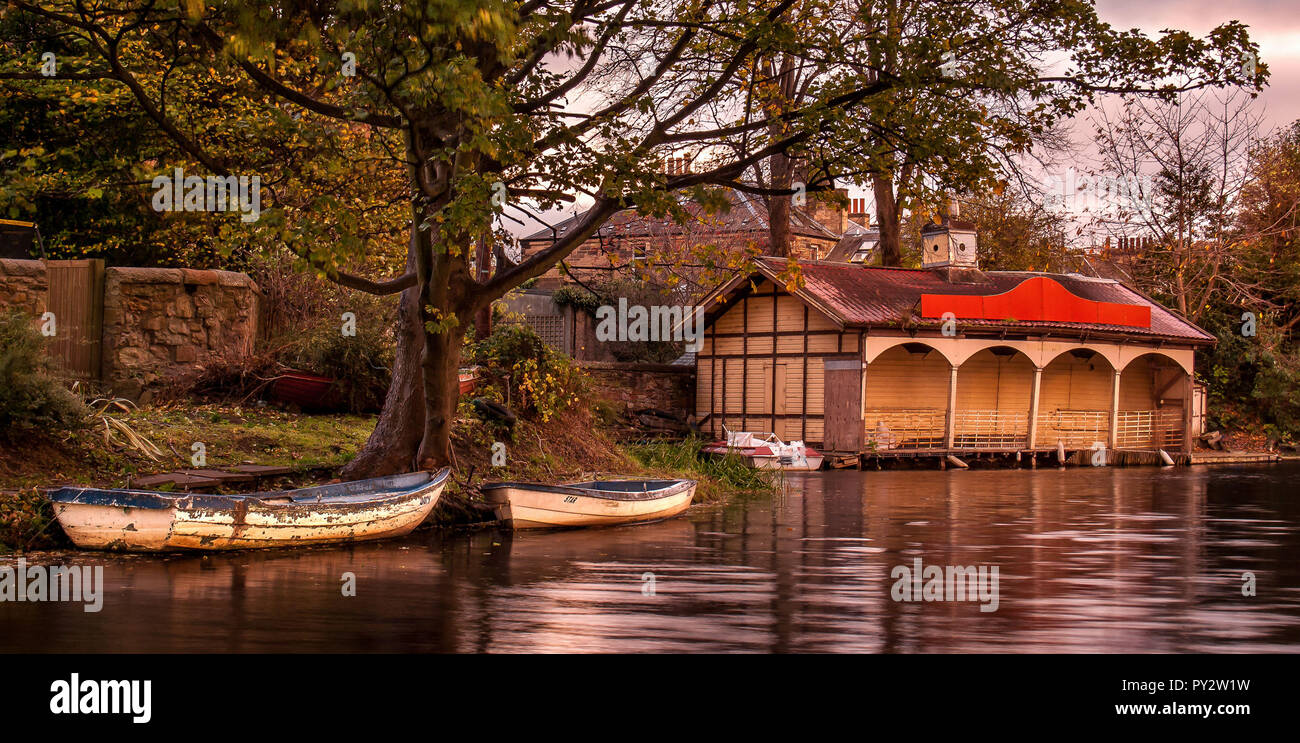 Une longue exposition d'Ashley Terrasse Boathouse, à Édimbourg, à l'automne lumière du soir avec de l'eau, deux barques et un arbre en premier plan Banque D'Images