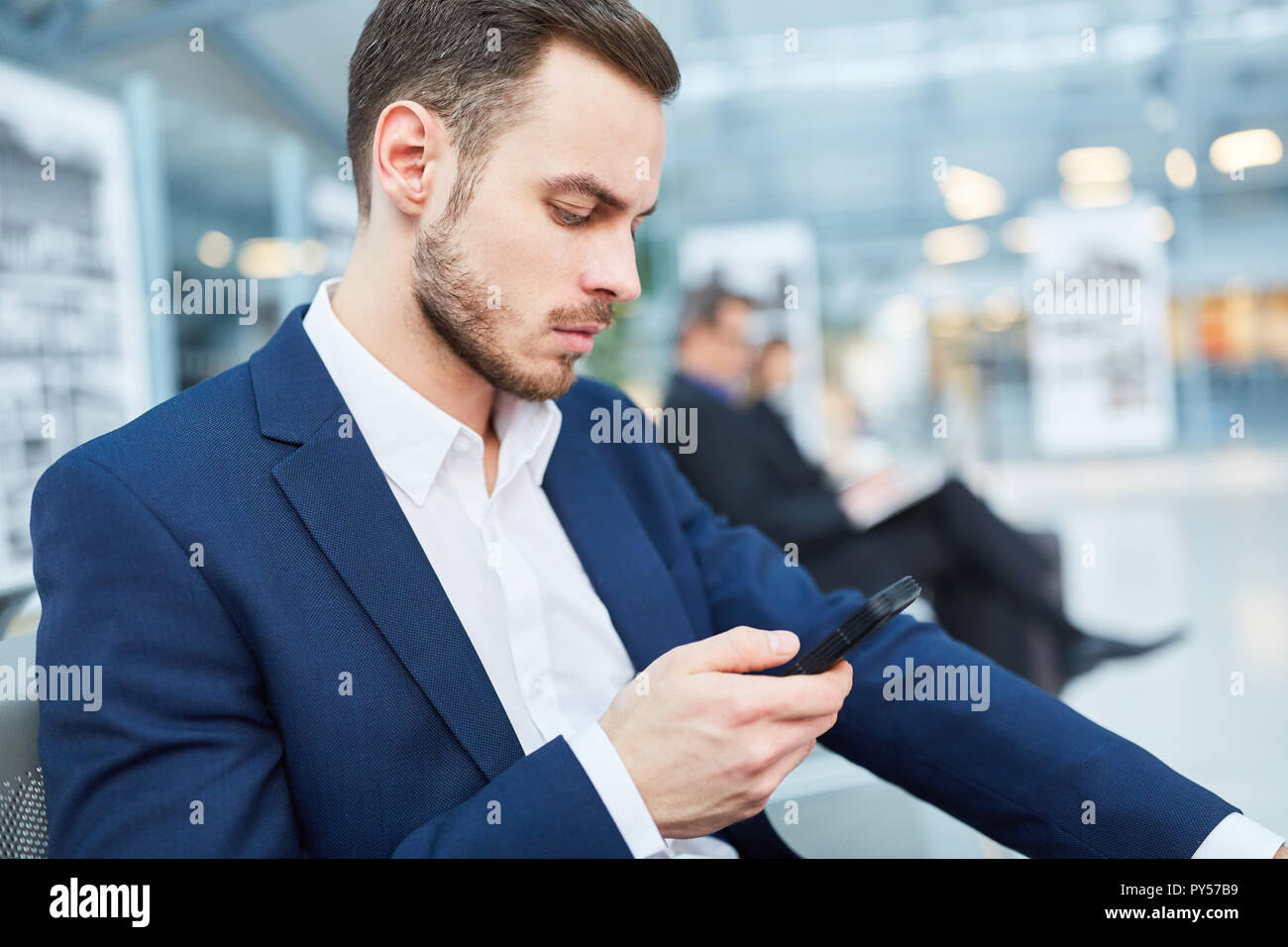 L'homme d'affaires en voyage d'affaires lit un message texte sur son smartphone à l'aéroport Banque D'Images
