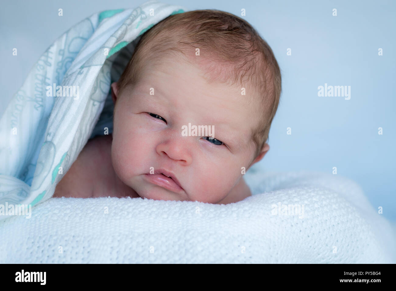 Bébé nouveau-né sur le ventre de pose à la recherche jusqu'à l'appareil photo avec une couverture sur la tête. Banque D'Images