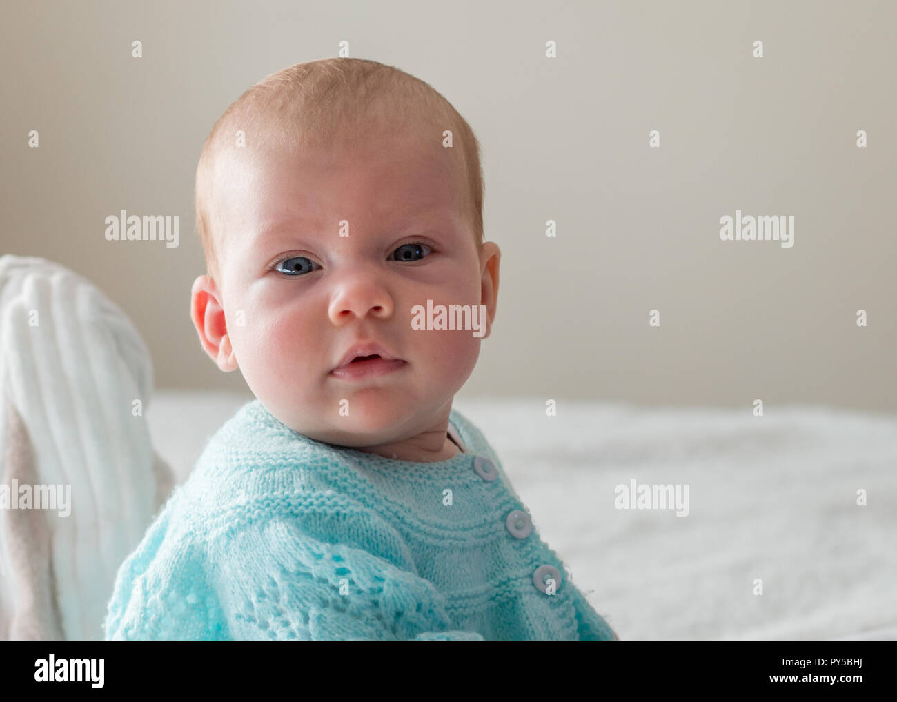 Petit bébé assis sur le lit et regardant la caméra close up of face portrait. Banque D'Images