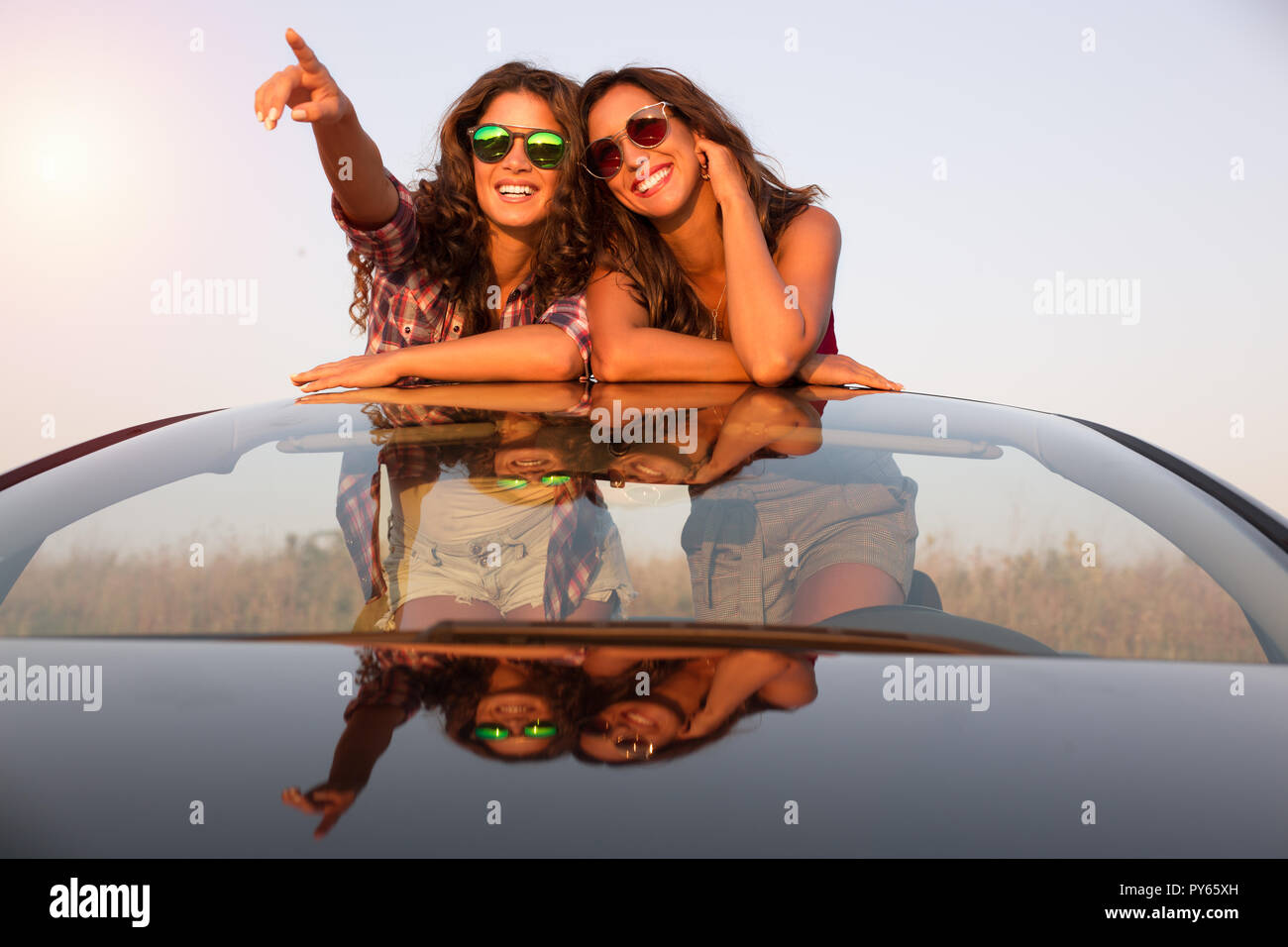 Deux belles jeunes filles avec des lunettes de soleil dans une voiture  décapotable regarde quelque chose au coucher du soleil Photo Stock - Alamy