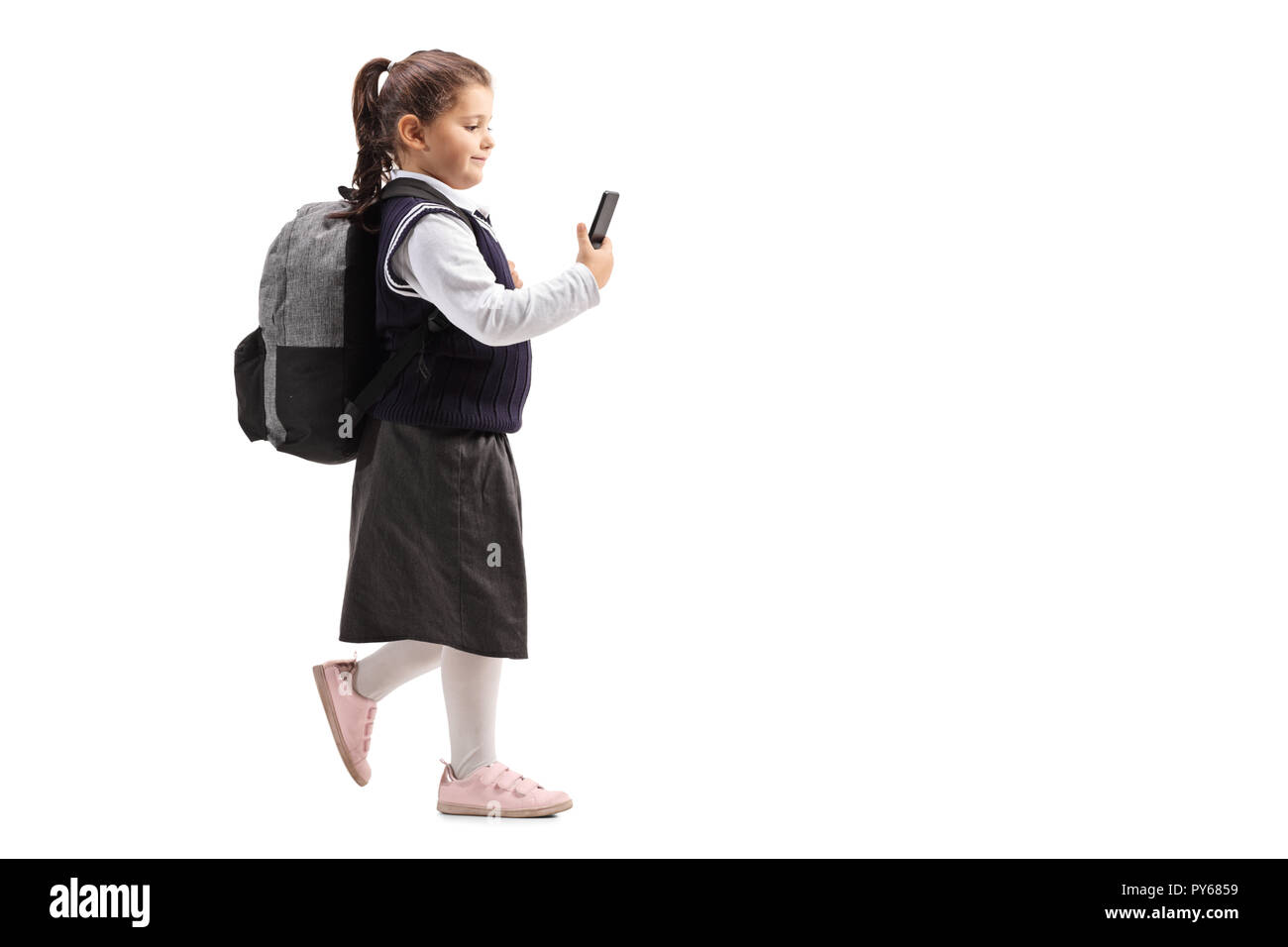 Longueur totale d'un coup peu lycéenne en uniforme à l'aide d'un téléphone mobile et la marche à pied isolé sur fond blanc Banque D'Images