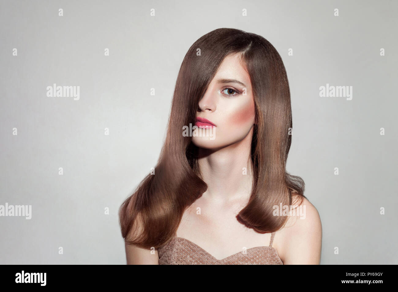 Portrait of attractive brunette woman avec maquillage lumineux et brillant tout droit de poils, posant sur fond gris isolé. piscine, studio shot on copie spa Banque D'Images