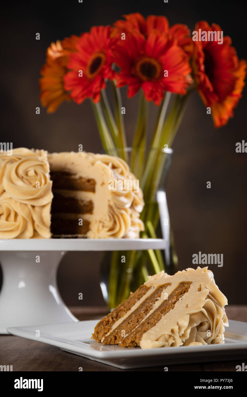 Tranche d'un gâteau aux épices citrouille à côté de l'ensemble du gâteau avec des fleurs d'automne orange. Banque D'Images