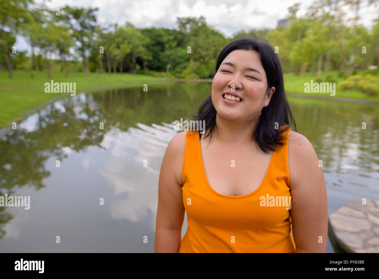 Belle femme asiatique de l'embonpoint en souriant avec les yeux fermé en park Banque D'Images
