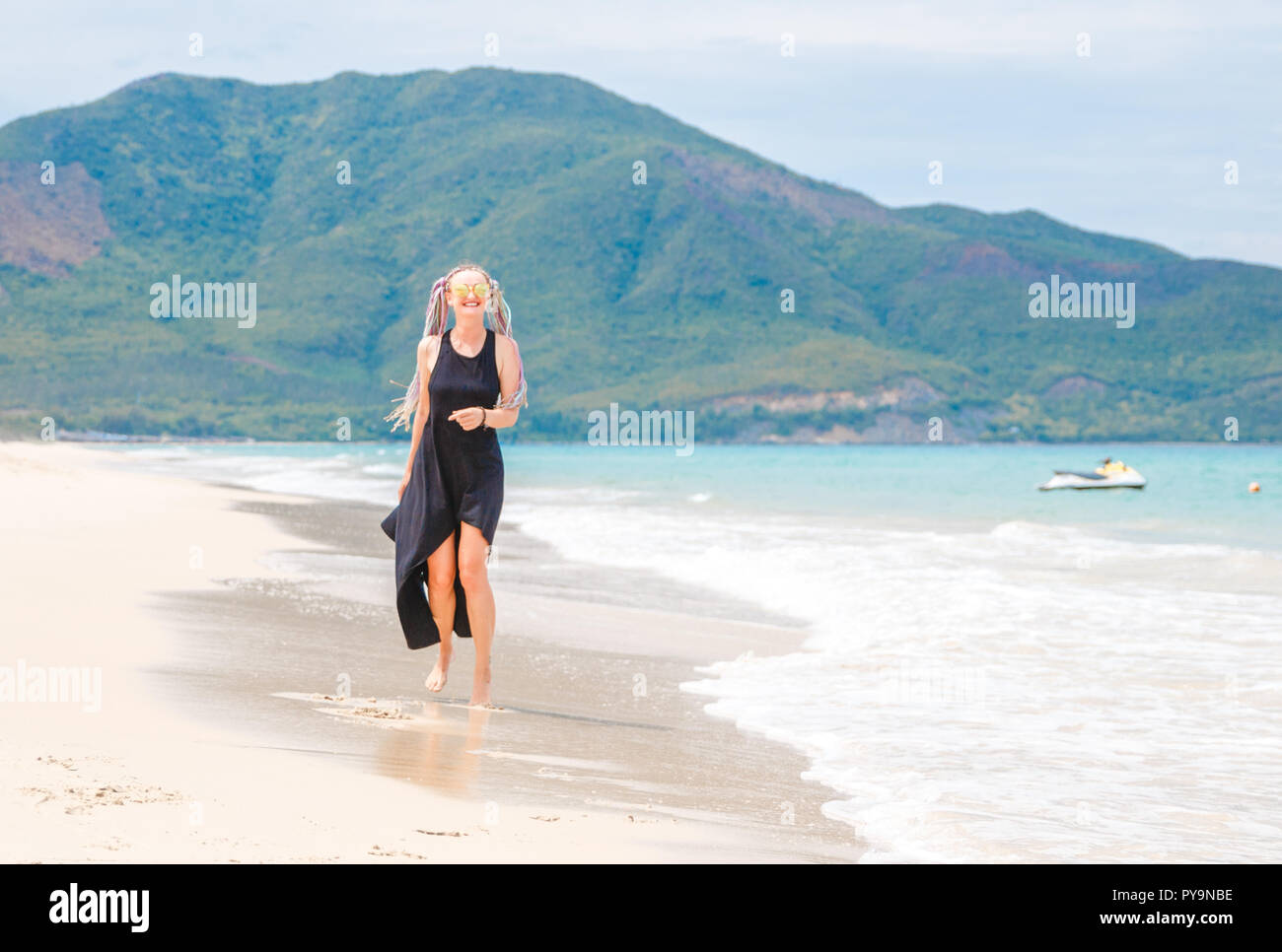 Belle jeune fille dans une robe noire promenades sur la plage. Banque D'Images
