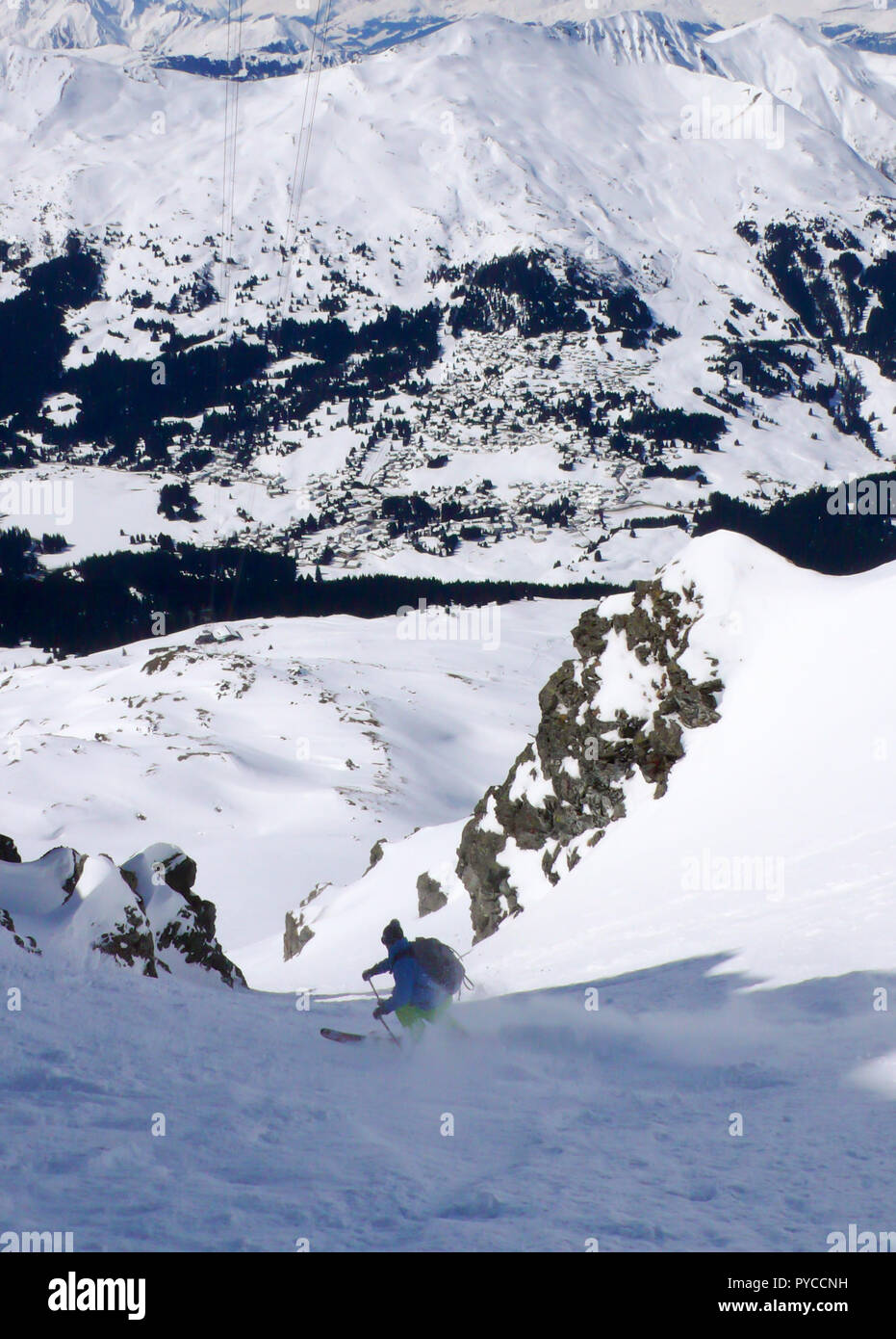 Ski skieur extrême vers le bas un étroit couloir de neige en vue de villages alpins loin dans la vallée ci-dessous en Suisse Banque D'Images