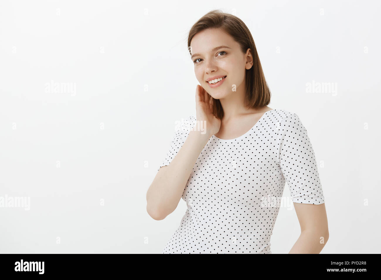 Mignon et heureux d'un collègue femelle en T-shirt, touchant doucement le cou et sourit joyeusement, tandis que l'article retourné demi-mur gris, sa timidité et le rougissement de compliment Banque D'Images