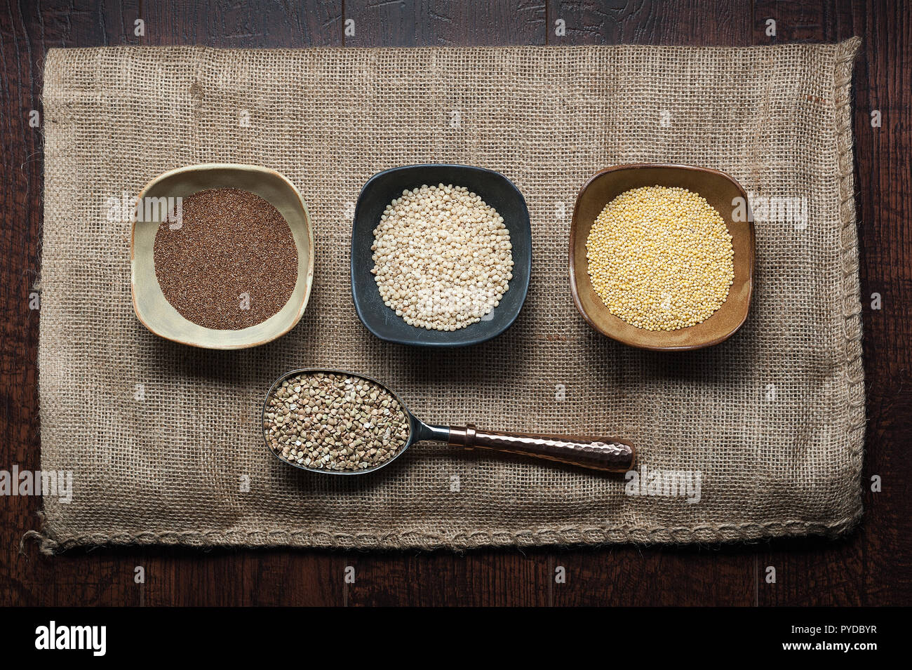 Grains anciens de teff, le sorgho, le millet et le sarrasin dans des bols et d'un scoop sur un sac de jute. Banque D'Images