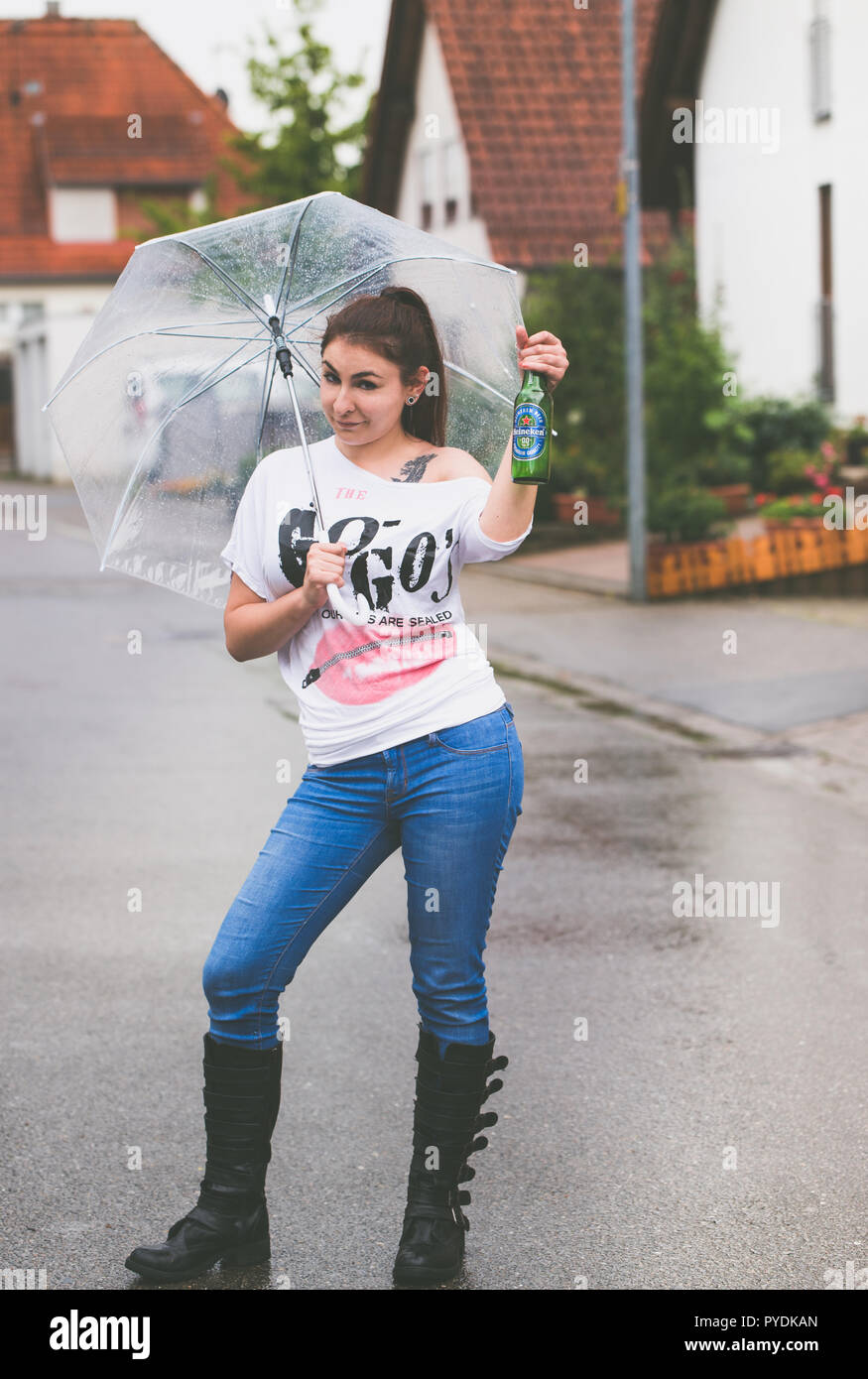 Une jeune femme avec un parapluie dans sa main des danses sous la pluie  tenant une bouteille de bière Heineken Photo Stock - Alamy