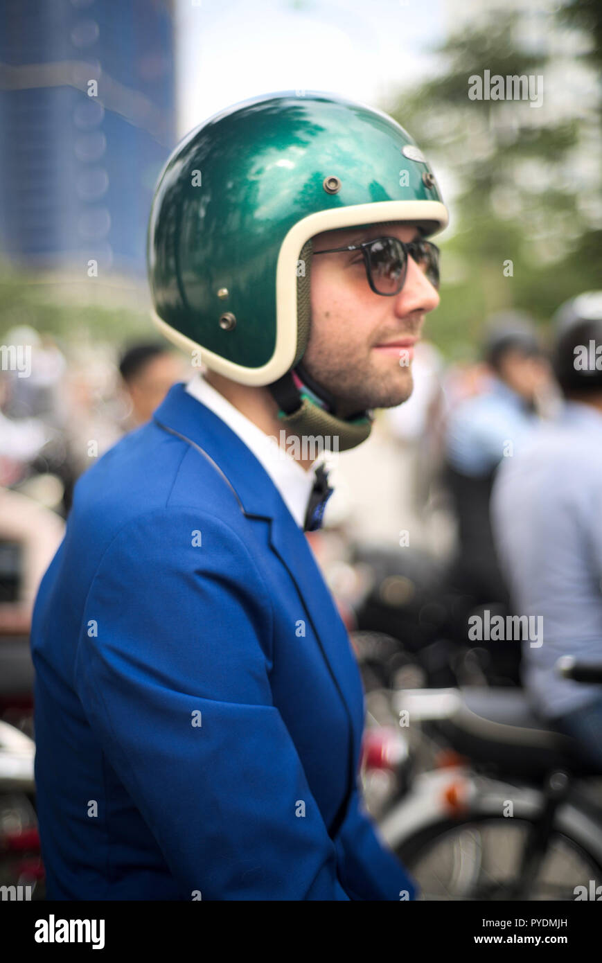 L'homme en costume bleu Causasian avec bowtie, lunettes et casque de moto avec foule en arrière-plan. Banque D'Images