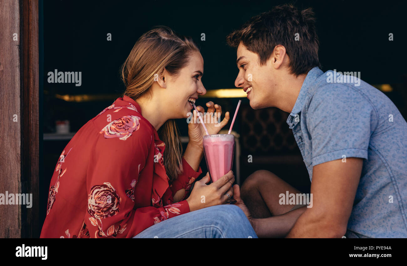 Couple heureux de boire un milkshake à deux pailles à la recherche à l'autre. Smiling man and woman on a date assis dans un restaurant et le partage d'un milkshake. Banque D'Images