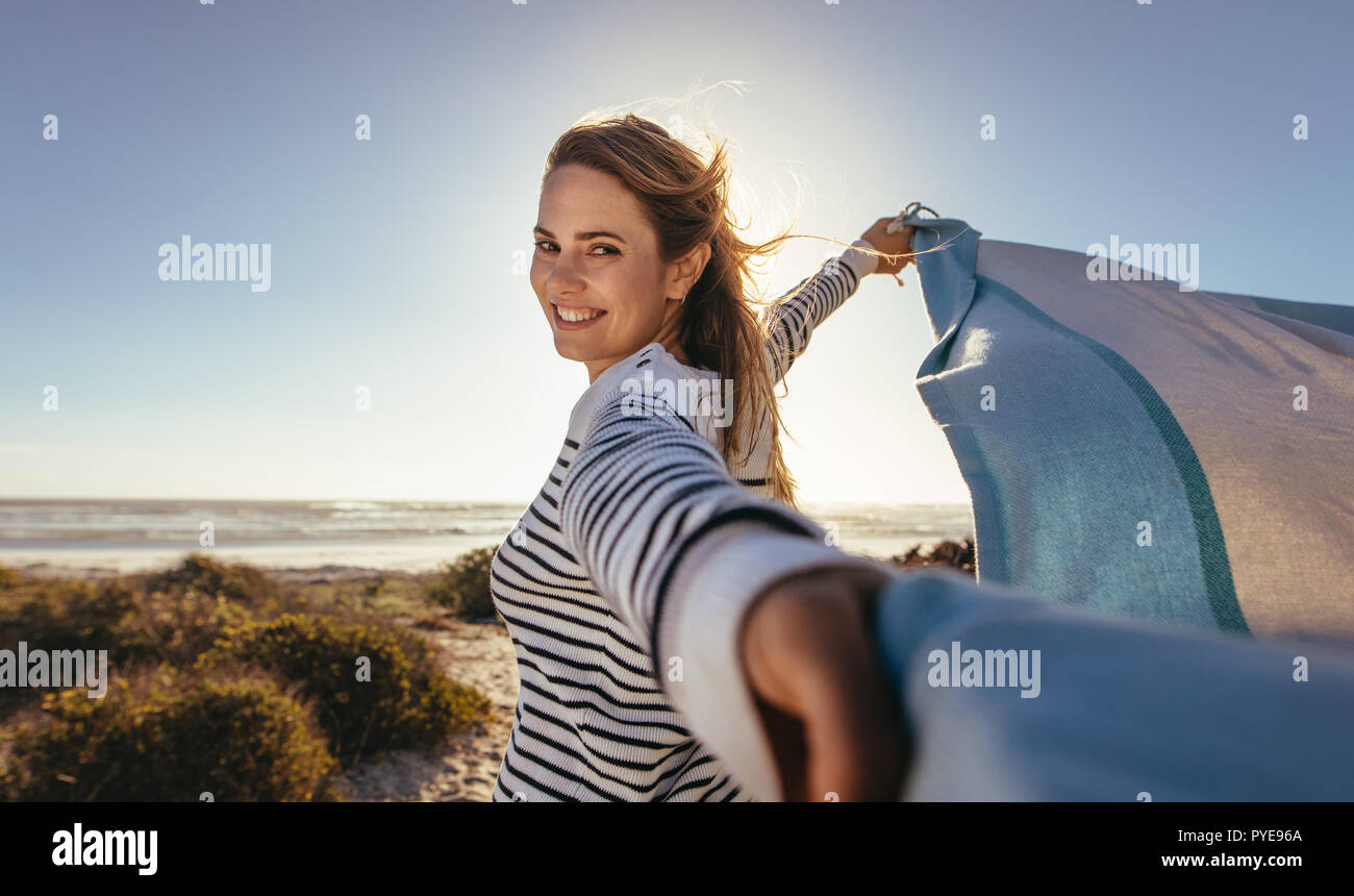 Portrait of a smiling woman holding a drape contre la brise de mer. Femme debout sur la plage tenant un chiffon volant à deux mains. Banque D'Images
