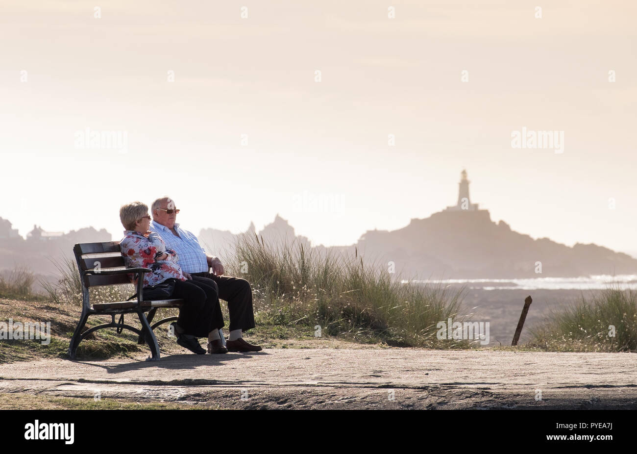 Un couple de personnes âgées se détendre sur un banc à St Ouen's Beach avec La Corbière lighthouse en arrière-plan, Jersey Banque D'Images