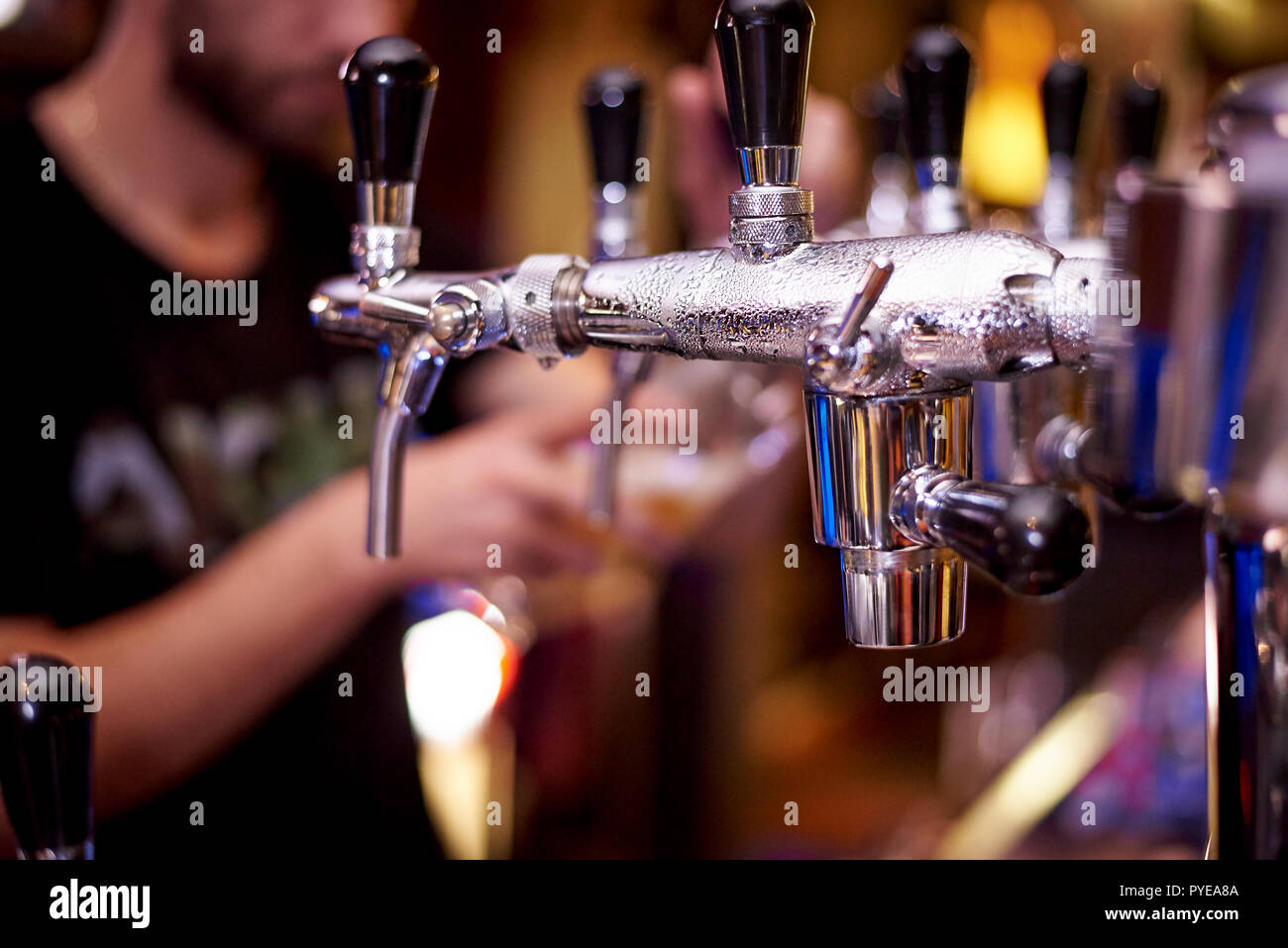 Appuyez sur la bière avec des gouttes sur un arrière-plan flou bartender pouring beer dans un verre. Banque D'Images