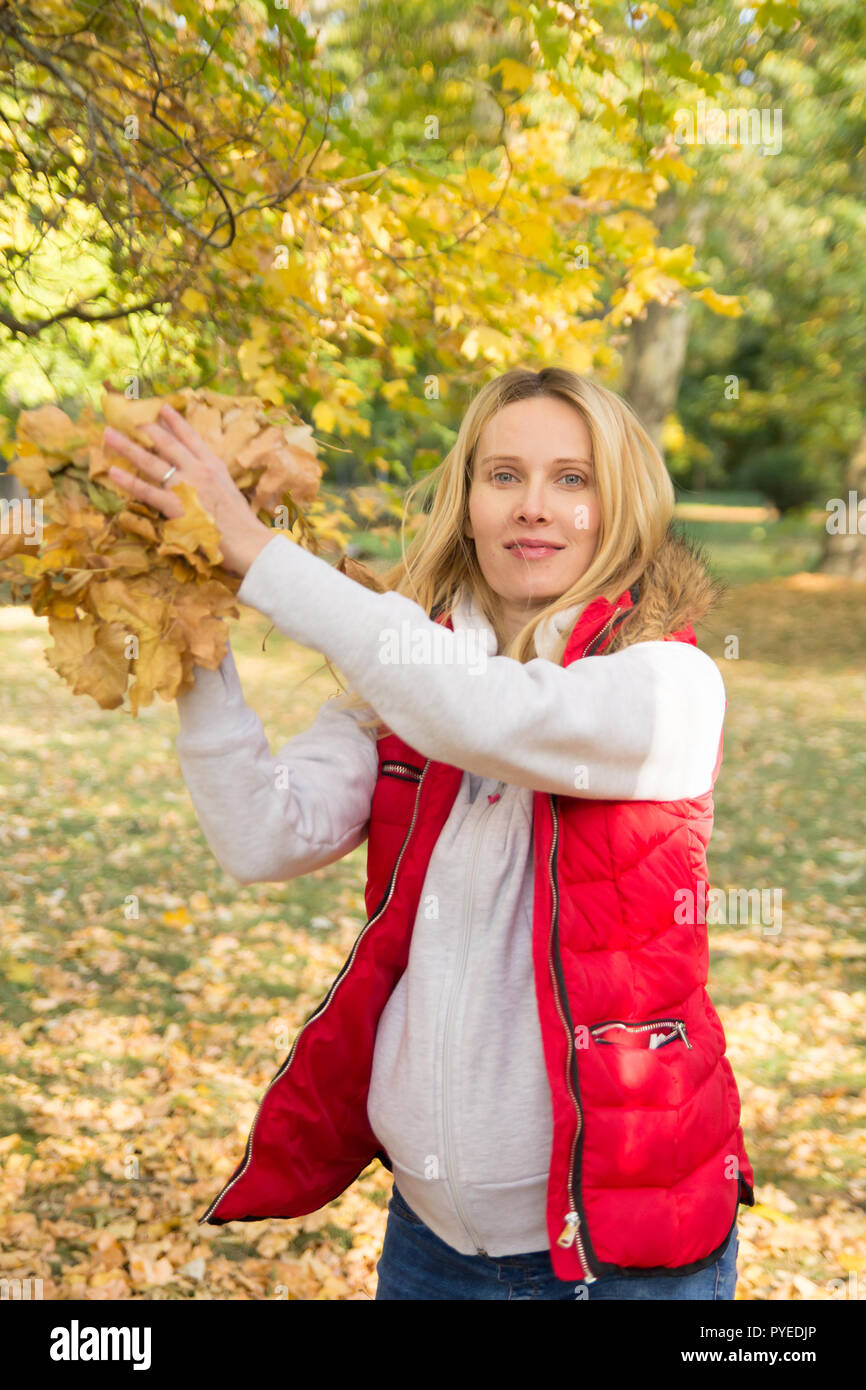 Cheerful young woman throwing leaves in autumn forest Banque D'Images