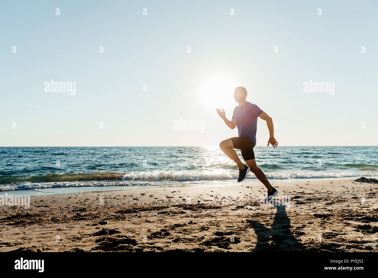 Runner homme courir le long de plage de sable fin dans le coucher du soleil Banque D'Images