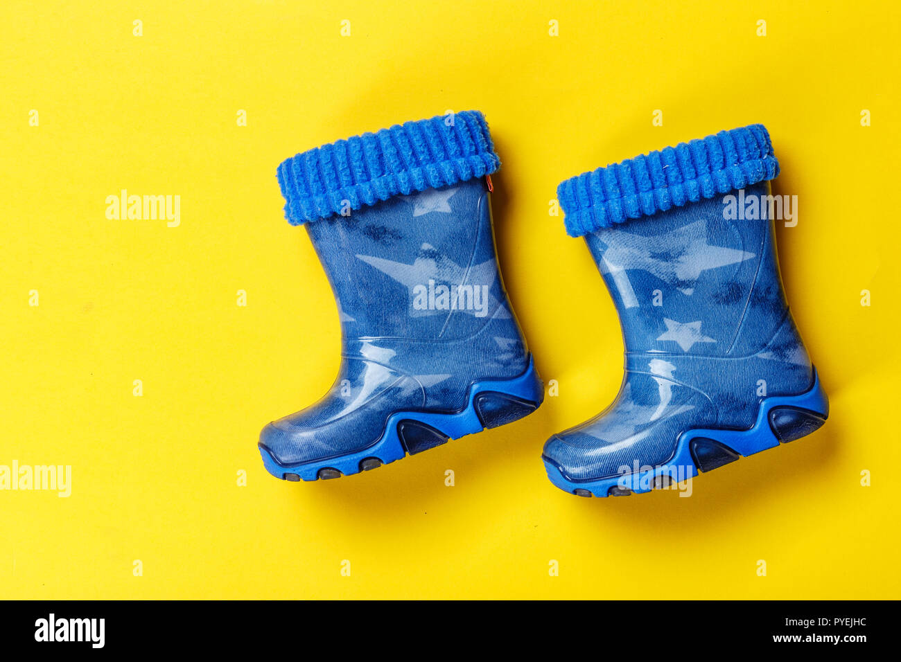 Une paire de bottes en caoutchouc bleu sur un petit garçon sur un fond jaune. chaussures d'automne Banque D'Images