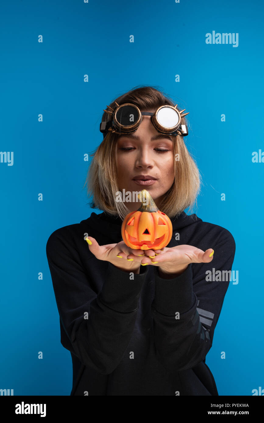 Femme portant des lunettes steampunk et black hoodie tenant une Halloween  citrouille sculptée. Steampunk goth à thème tournage en studio contre fond  bleu Photo Stock - Alamy