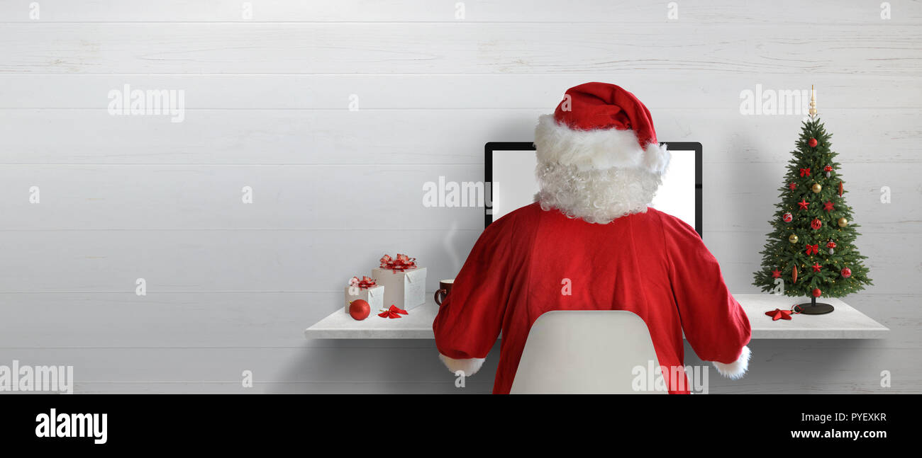 Santa Claus travaillant sur un ordinateur dans son bureau durant les vacances de Noël. L'espace vide sur le mur pour le texte. Banque D'Images