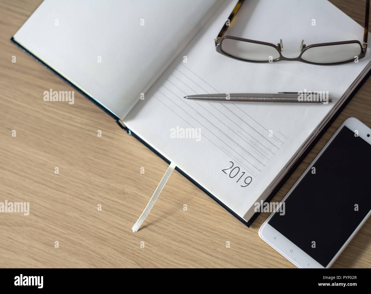 Nouvelle année 2019. Organiseur de bureau Calendrier, smartphone, lunettes et stylo-bille en argent sur un bureau en bois. Focus sélectif. Banque D'Images