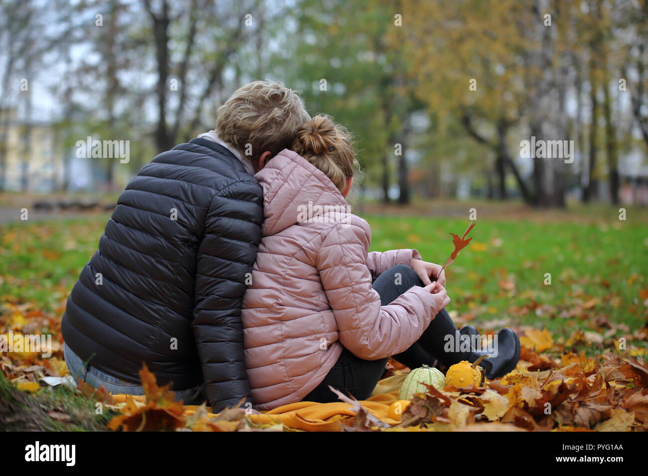 Mère et fille, les cheveux blonds, s'asseoir sur le sol, près de l'un l'autre, avec de bonnes émotions, sentiments, dans l'automne automne / parc, sur leur dos. Banque D'Images