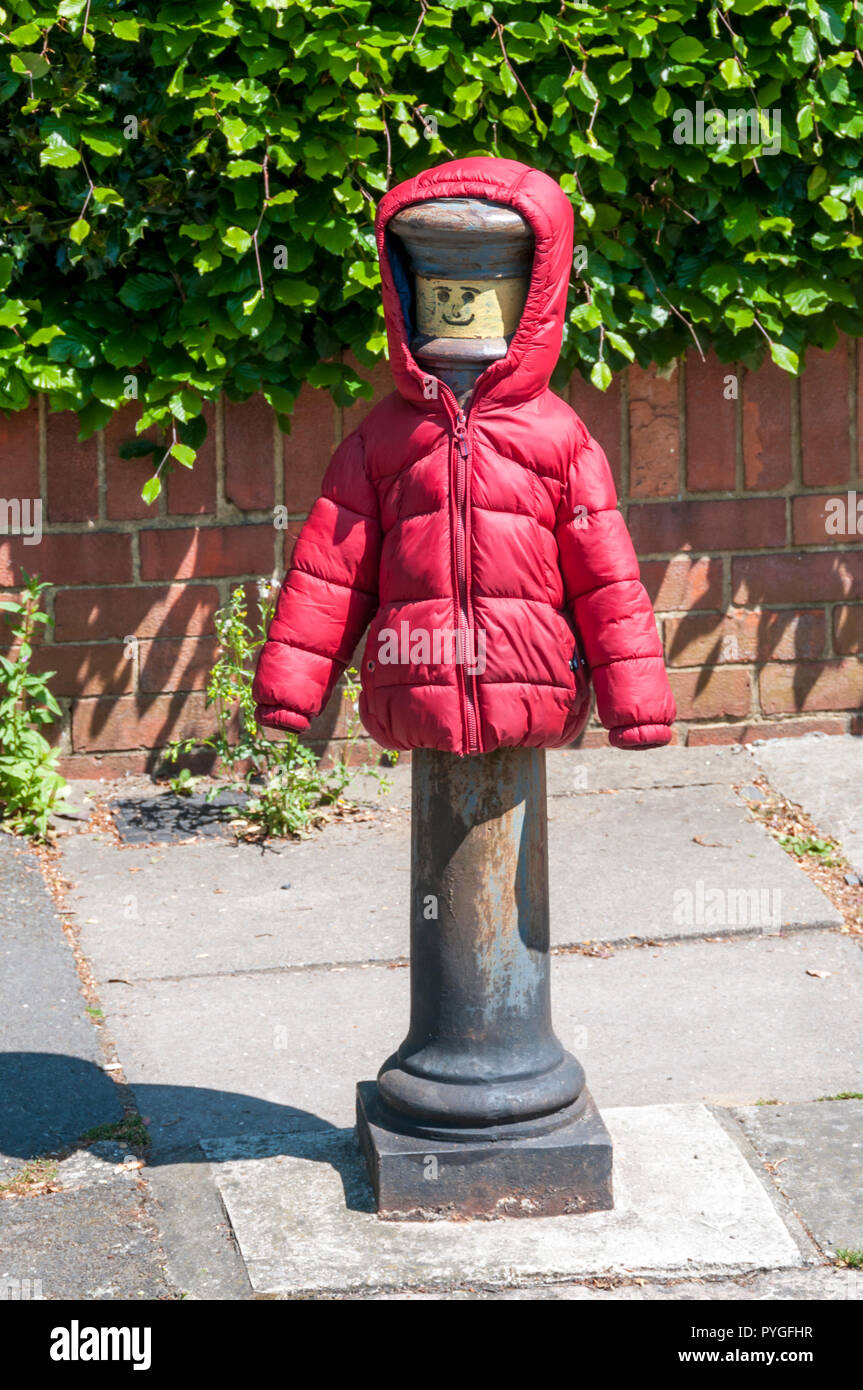 Un bollard à visage humain dessiné dessus et vêtu d'un anorak Banque D'Images