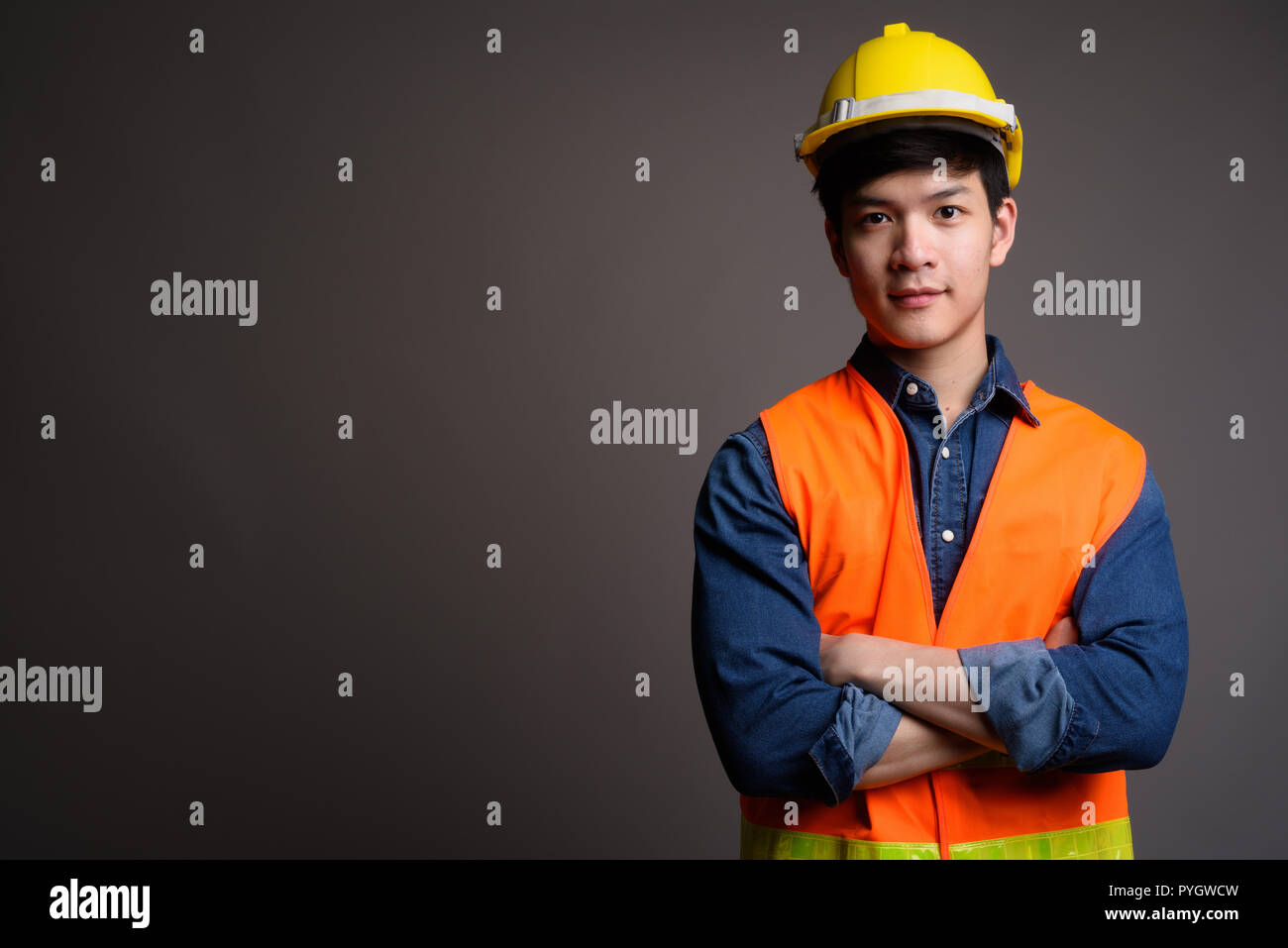 Beau jeune homme asiatique travailleur de la construction contre zone grise Banque D'Images