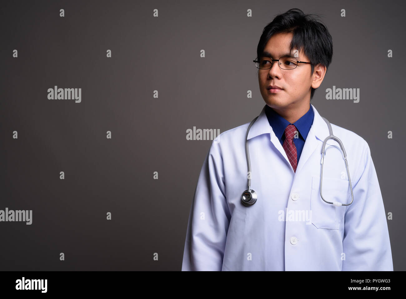 Portrait of young Asian man médecin pense contre l'arrière-plan gris Banque D'Images