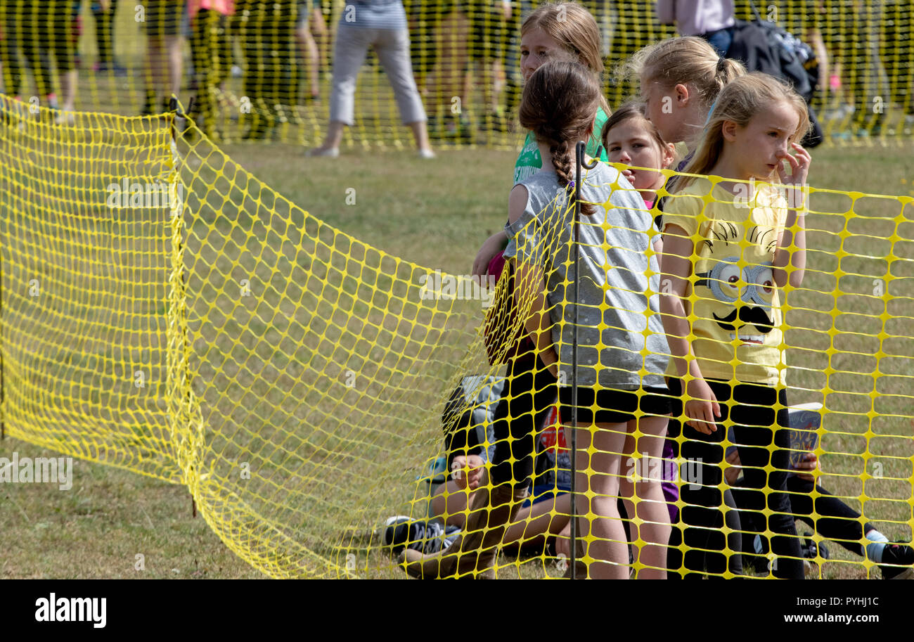 Certaines jeunes filles derrière un grillage de séparation en plastique jaune en attente d'une course d'obstacles course pour passer Banque D'Images