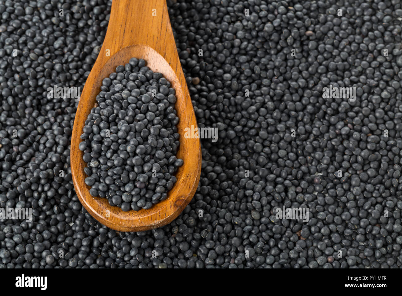 Tas de lentilles beluga bio noir en cuillère en bois noir sur fond de lentilles béluga Banque D'Images