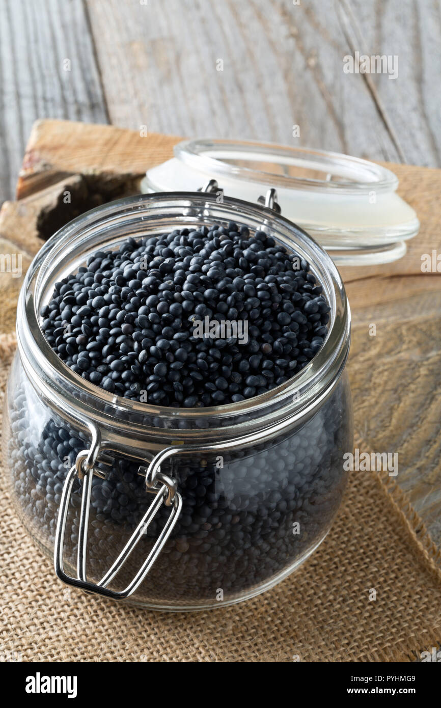 Tas de lentilles beluga bio noir en Pot de rangement sur l'arrière-plan de table en bois rustique Banque D'Images