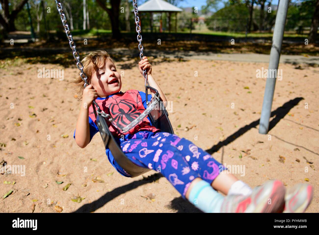 Un jeune enfant joue sur une balançoire dans un spiderman top, Ross River area, Townsville, Queensland, Australie Banque D'Images