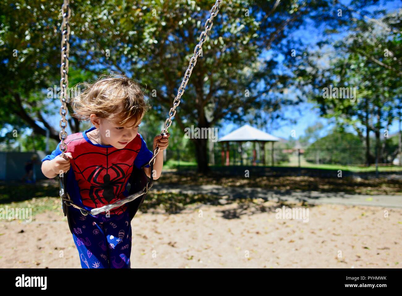 Un jeune enfant joue sur une balançoire dans un spiderman top, Ross River area, Townsville, Queensland, Australie Banque D'Images